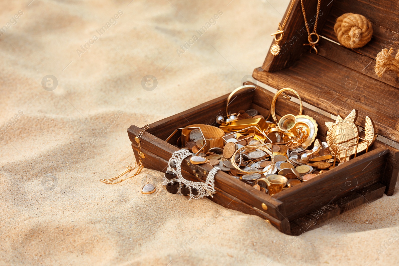 Photo of Open wooden treasure chest on sand, space for text