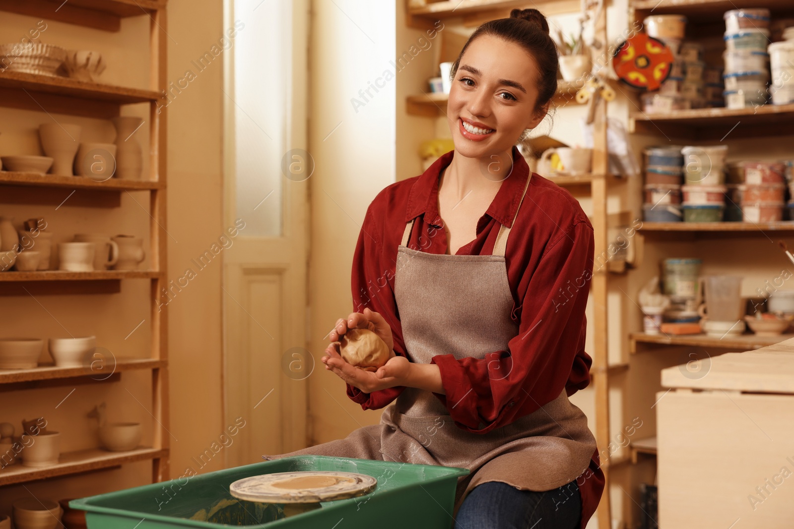 Photo of Happy woman crafting with clay over potter's wheel in workshop