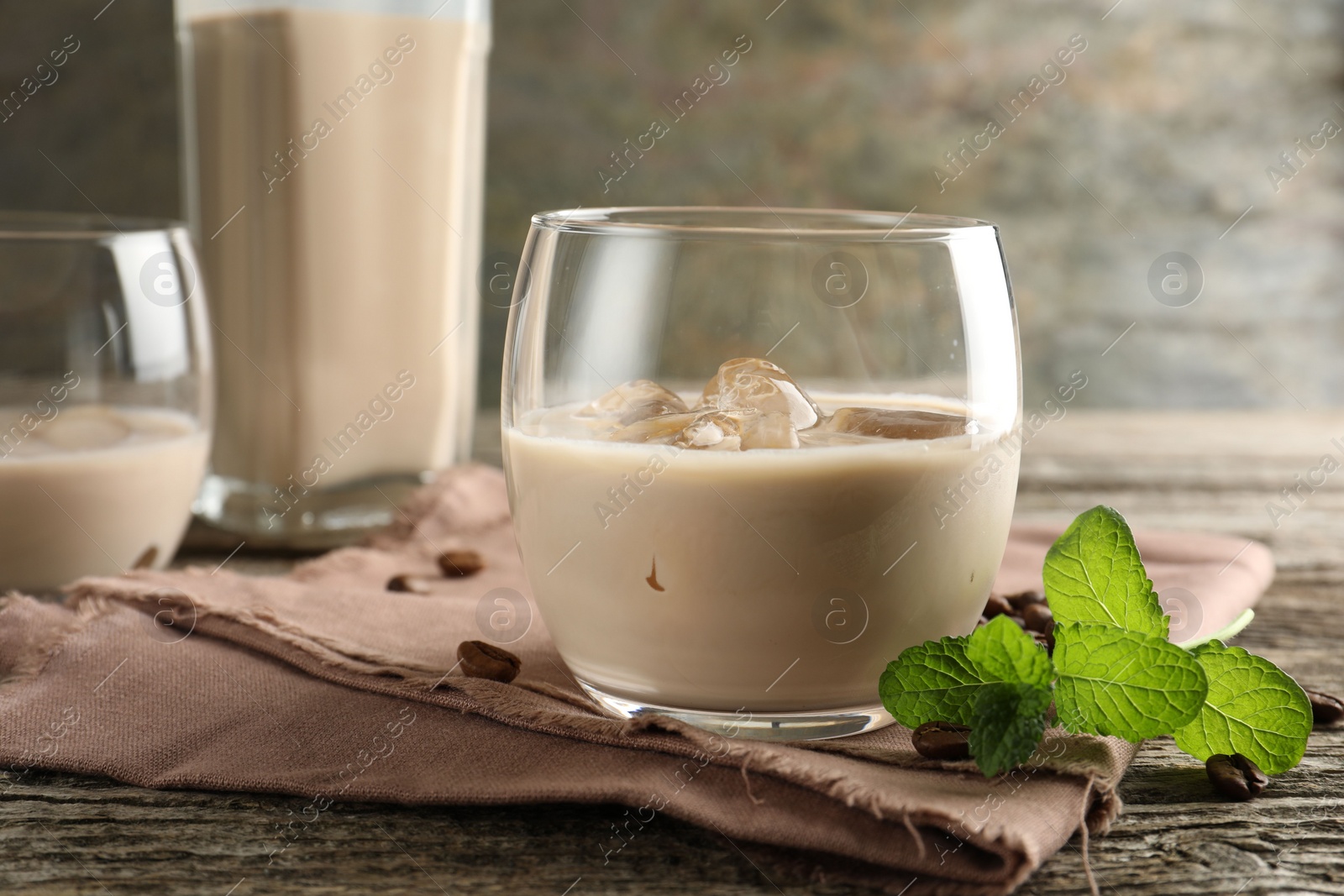 Photo of Coffee cream liqueur in glass, mint and beans on wooden table, closeup