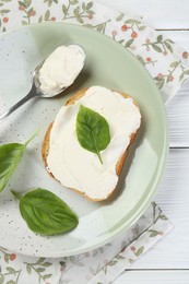 Photo of Delicious sandwich with cream cheese and basil leaves on white wooden table, top view