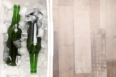 Photo of Plastic cool box with ice cubes and beer on wooden floor, top view. Space for text
