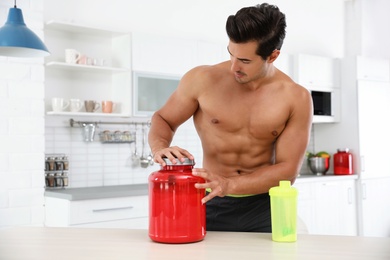 Photo of Young shirtless athletic man preparing protein shake in kitchen