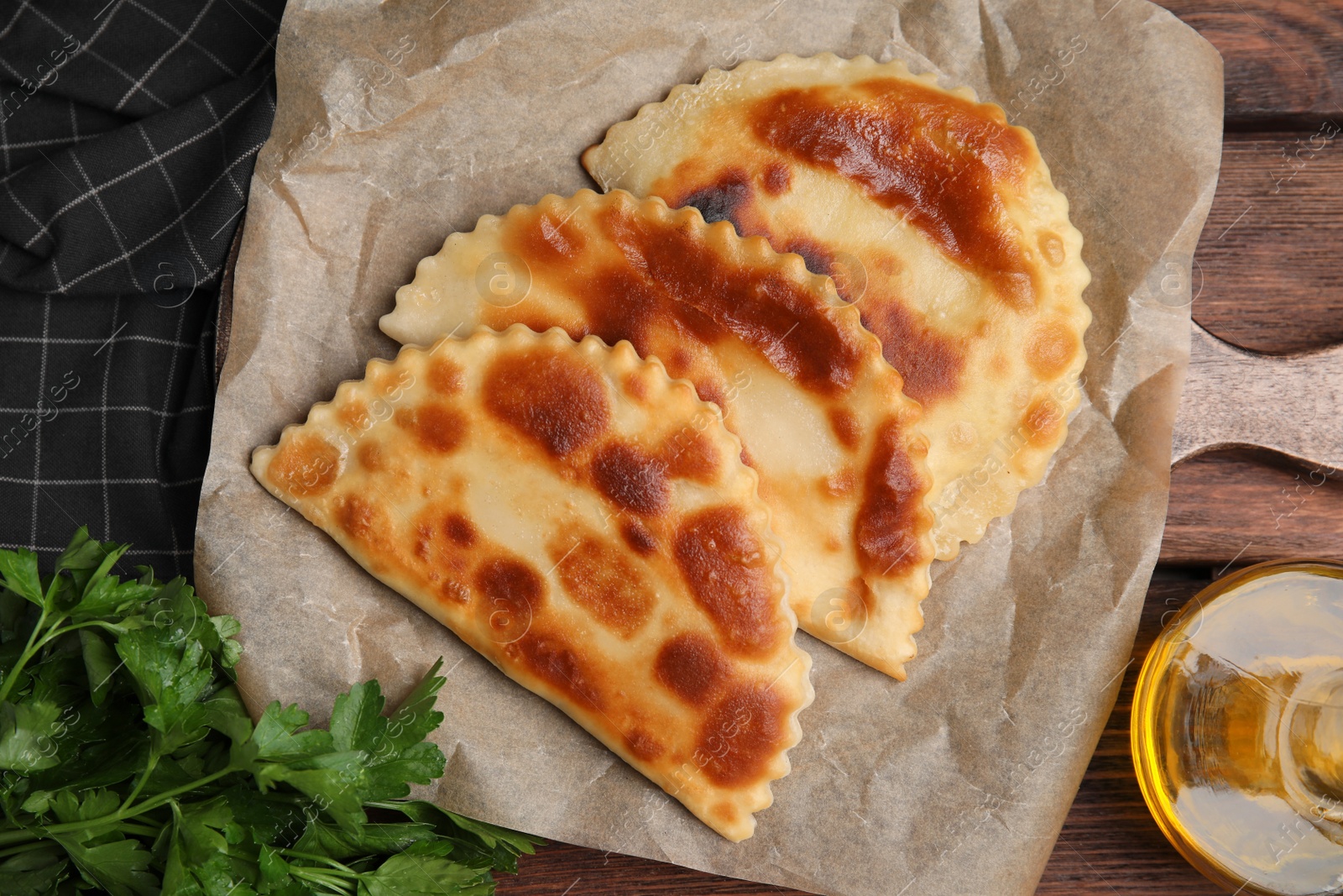 Photo of Board with delicious fried chebureki and parsley on wooden table, flat lay