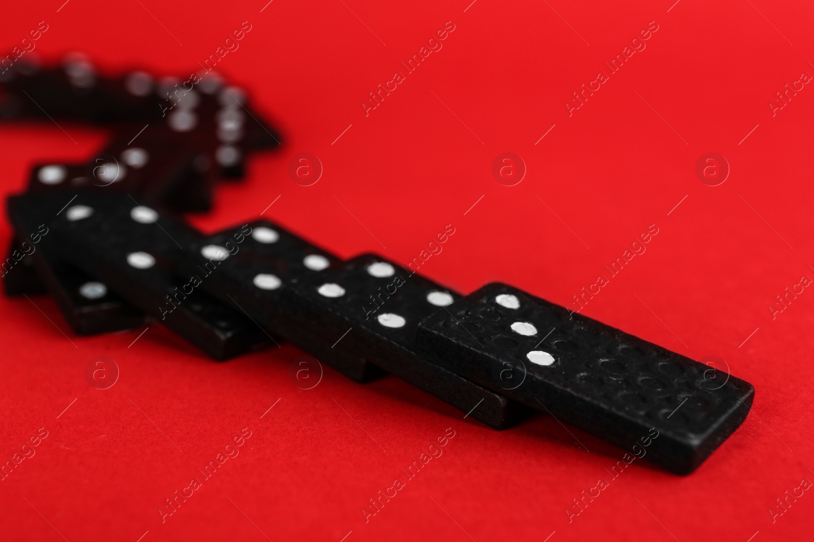 Photo of Fallen black domino tiles on red background. Space for text