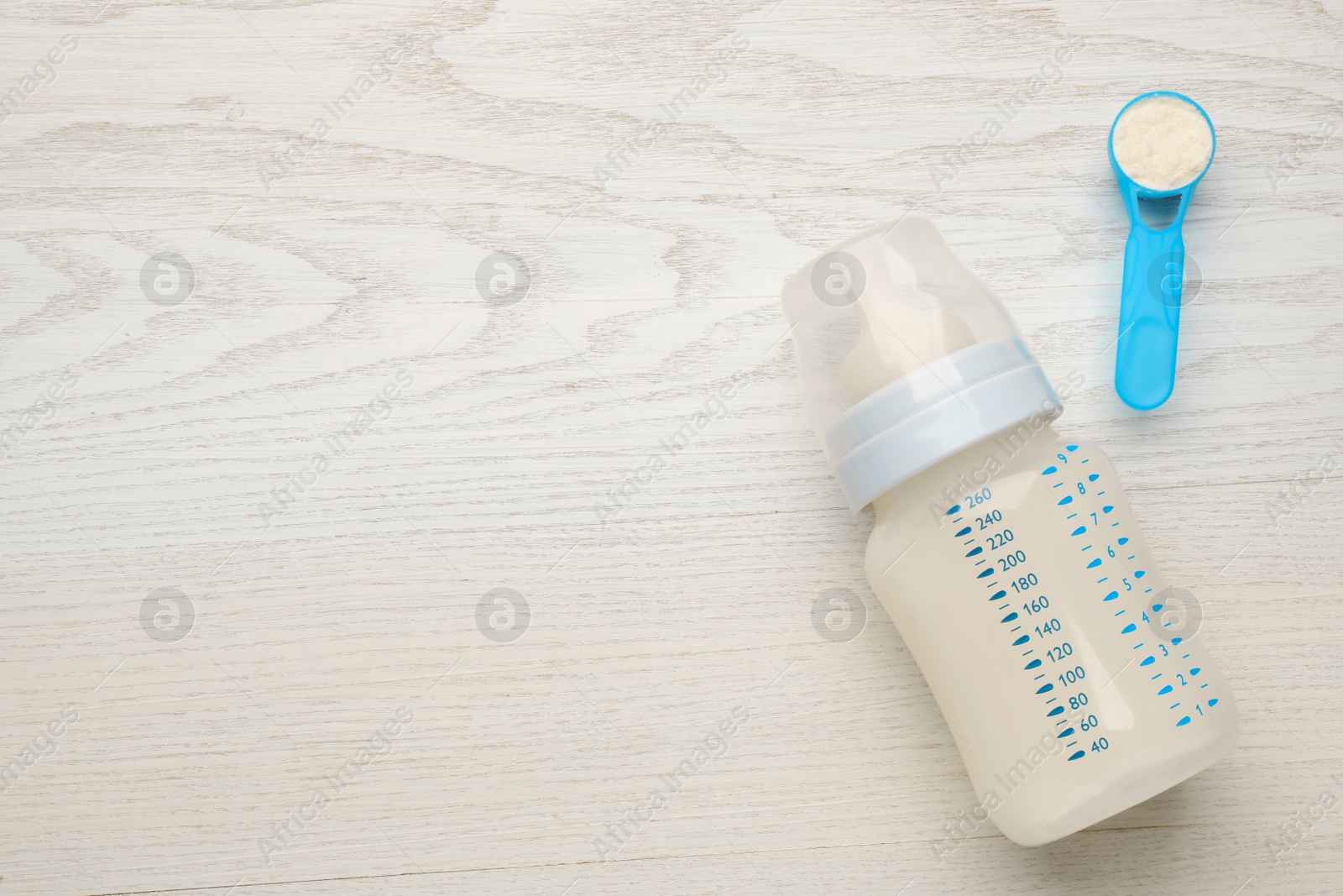 Photo of Feeding bottle with infant formula and powder on white wooden table, flat lay. Space for text