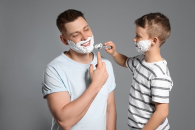 Son applying shaving foam on dad's face, grey background