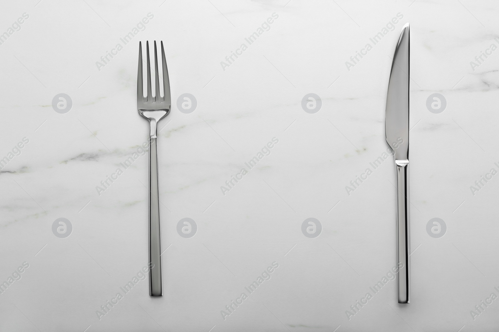 Photo of Shiny fork and knife on white marble table, flat lay. Space for text