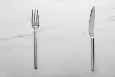 Photo of Shiny fork and knife on white marble table, flat lay. Space for text