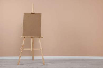 Wooden easel with blank board near beige wall indoors. Space for text