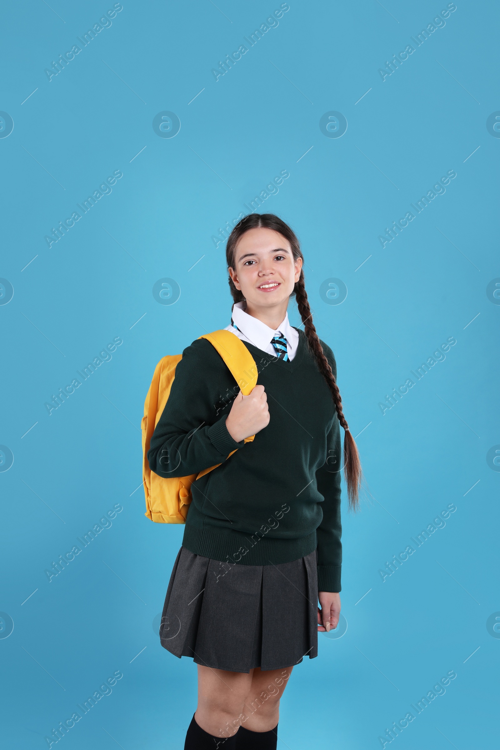 Photo of Teenage girl in school uniform with backpack on light blue background