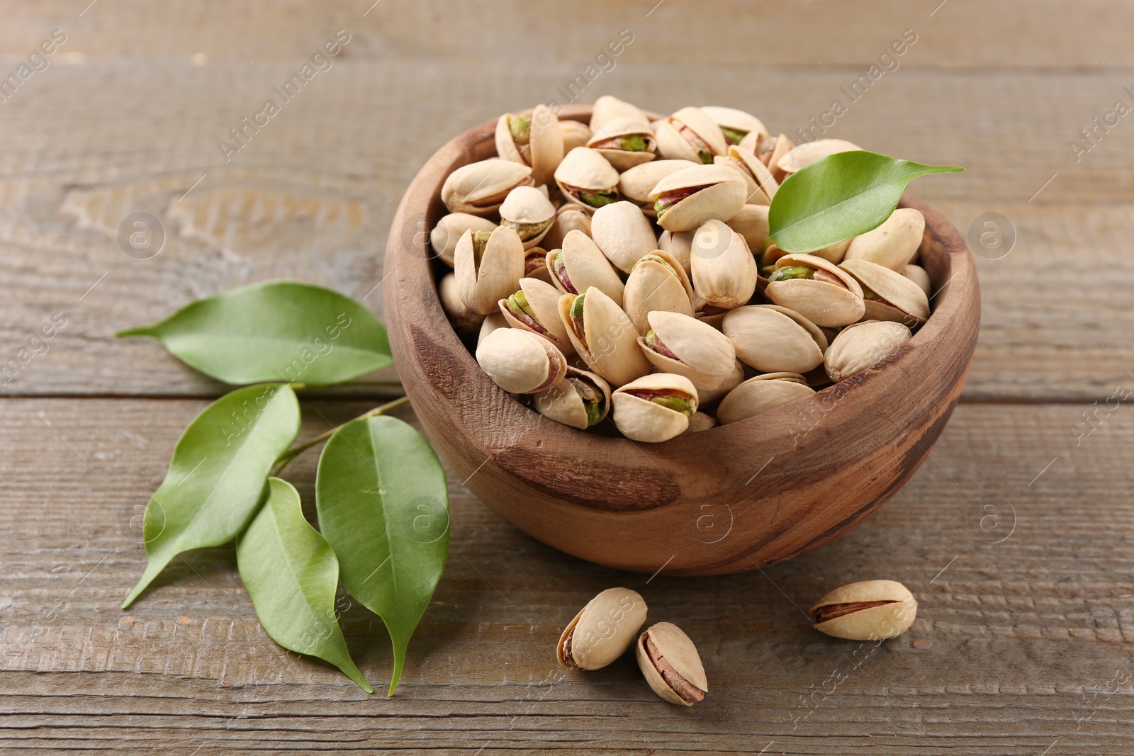 Photo of Delicious pistachios in bowl on wooden table