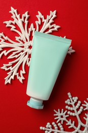 Photo of Tube of hand cream and snowflakes on red background, flat lay. Winter skin care