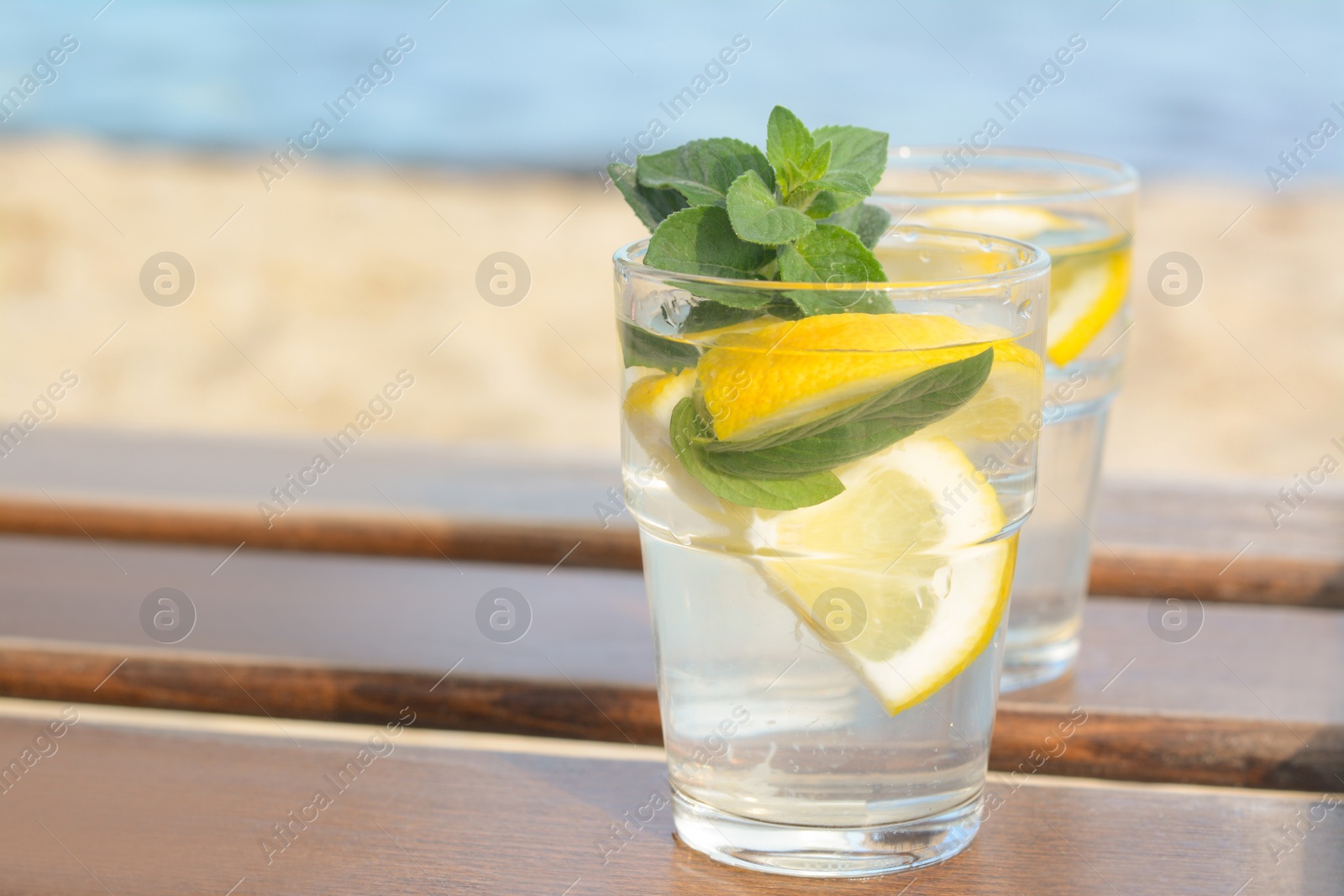 Photo of Refreshing water with lemon and mint on wooden table outdoors. Space for text