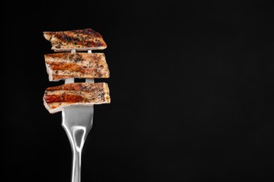 Photo of Meat fork with pieces of delicious grilled pork steak against black background, space for text