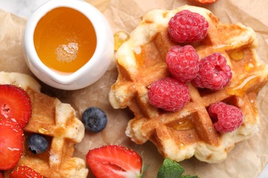 Photo of Delicious Belgian waffles with fresh berries and honey on parchment paper, top view