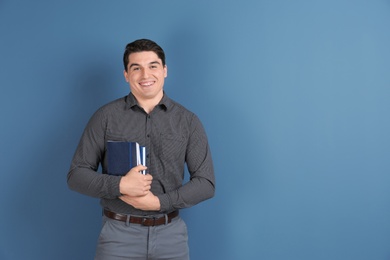 Portrait of male teacher with notebooks on color background