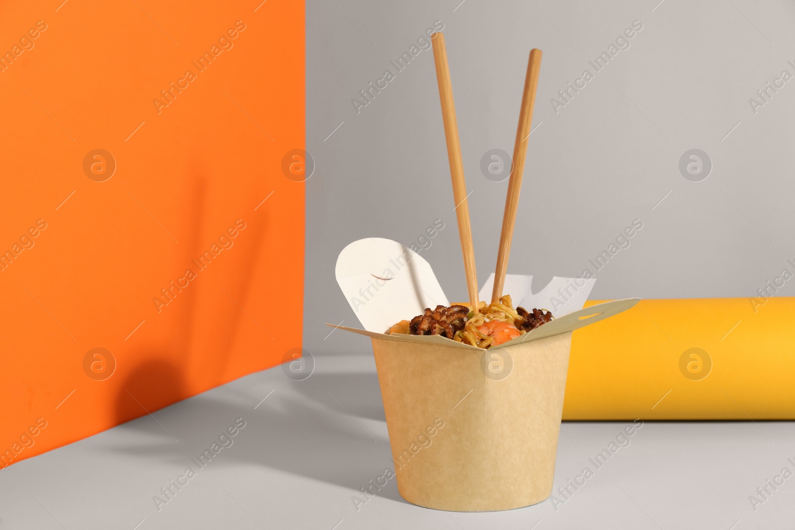 Photo of Box of wok noodles with seafood and chopsticks on color background. Space for text