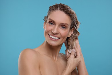 Portrait of beautiful happy woman washing hair on light blue background