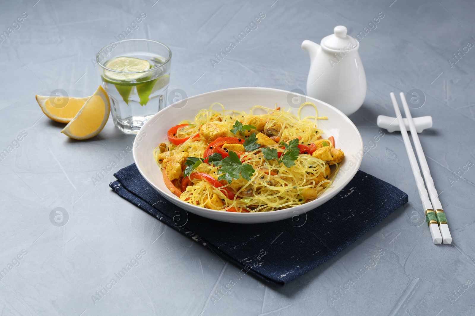 Photo of Stir-fry. Delicious cooked noodles with chicken and vegetables in bowl served on gray textured table