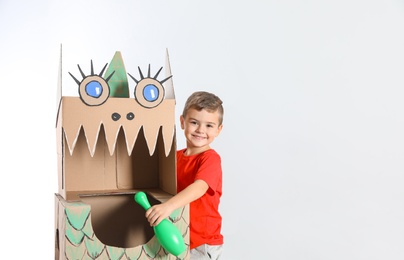 Photo of Cute little boy playing with cardboard dragon on white background. Space for text