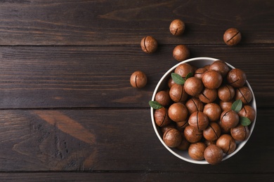 Photo of Bowl with organic Macadamia nuts and space for text on wooden background, top view