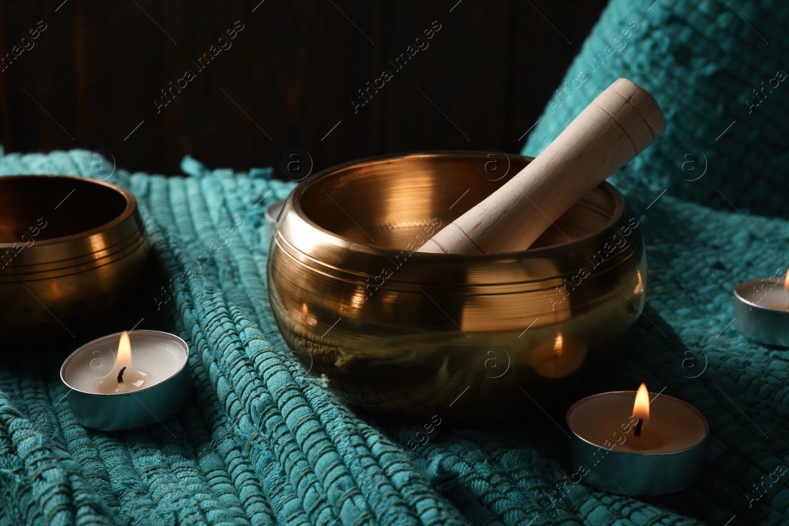 Photo of Tibetan singing bowls with mallet and burning candles on turquoise fabric