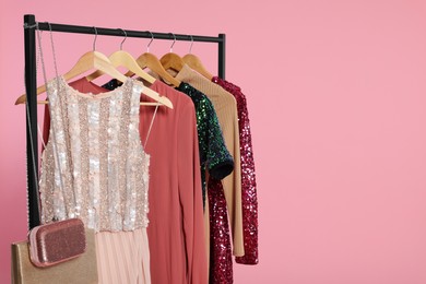 Photo of Rack with stylish women's clothes on wooden hangers and accessories against pink background, space for text