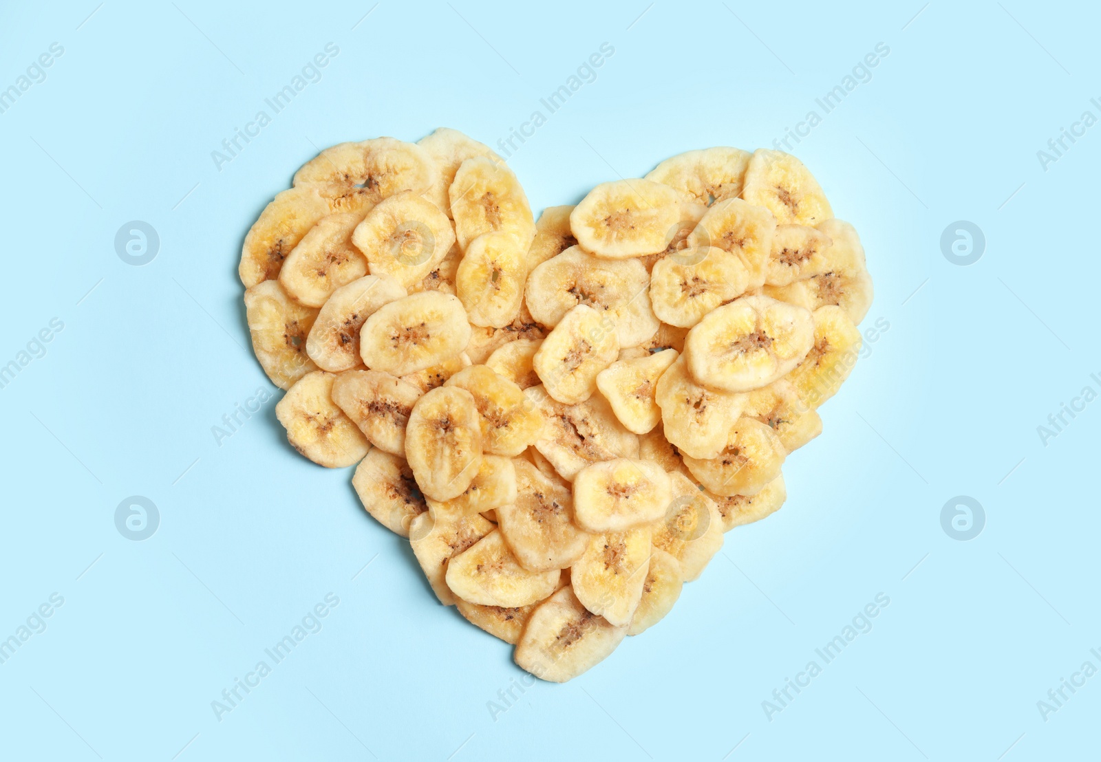 Photo of Heart shaped heap of sweet banana slices on color background, top view. Dried fruit as healthy snack