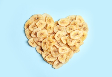 Photo of Heart shaped heap of sweet banana slices on color background, top view. Dried fruit as healthy snack