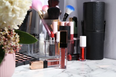 Bright lip glosses among different cosmetic products on white dressing table