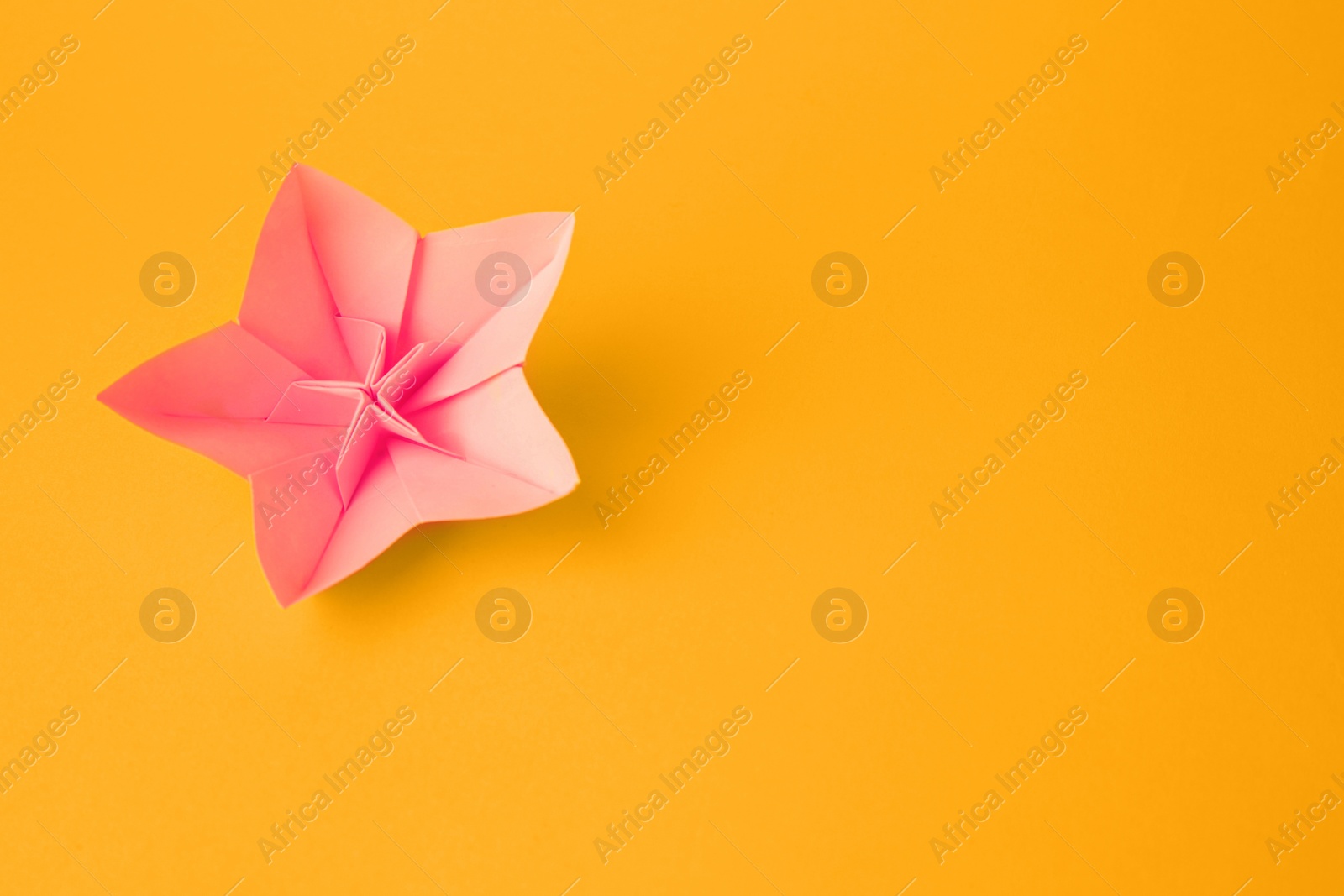 Photo of Origami art. Handmade pink paper flower on yellow background, top view with space for text