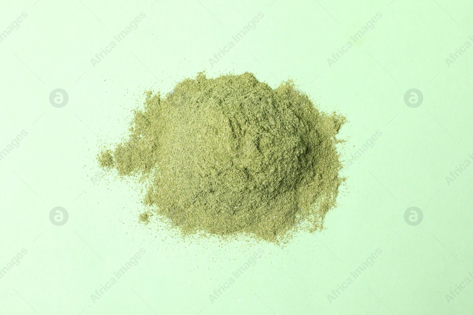 Photo of Pile of wheat grass powder on green table, top view
