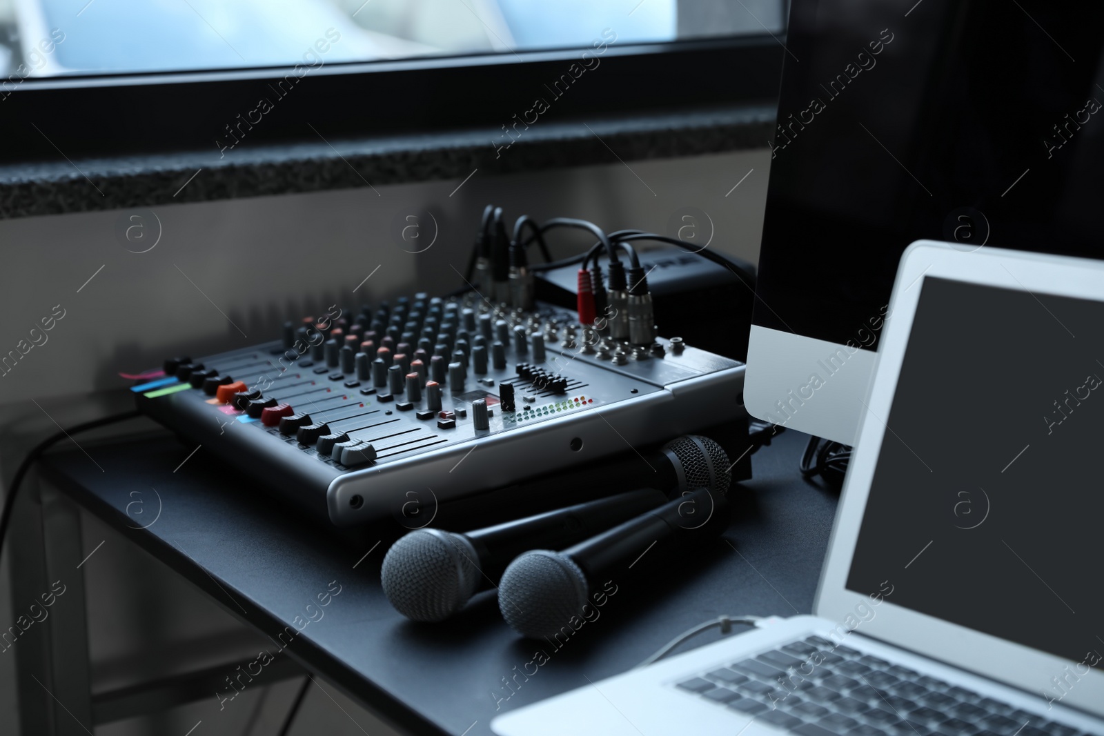 Photo of Modern audio mixing console and microphones on black table indoors. Music equipment