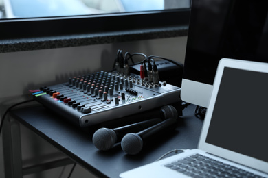 Photo of Modern audio mixing console and microphones on black table indoors. Music equipment