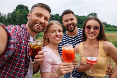 Photo of Happy friends with glasses of cocktails taking selfie outdoors
