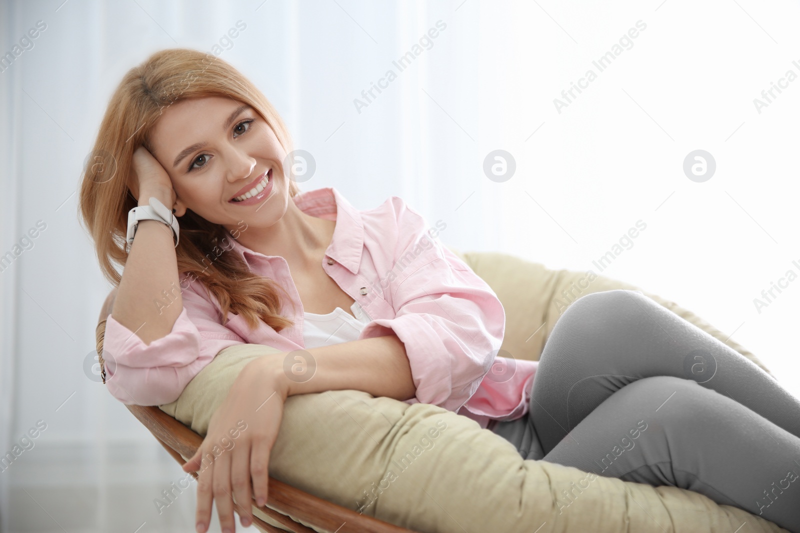 Photo of Young woman relaxing in papasan chair near window at home