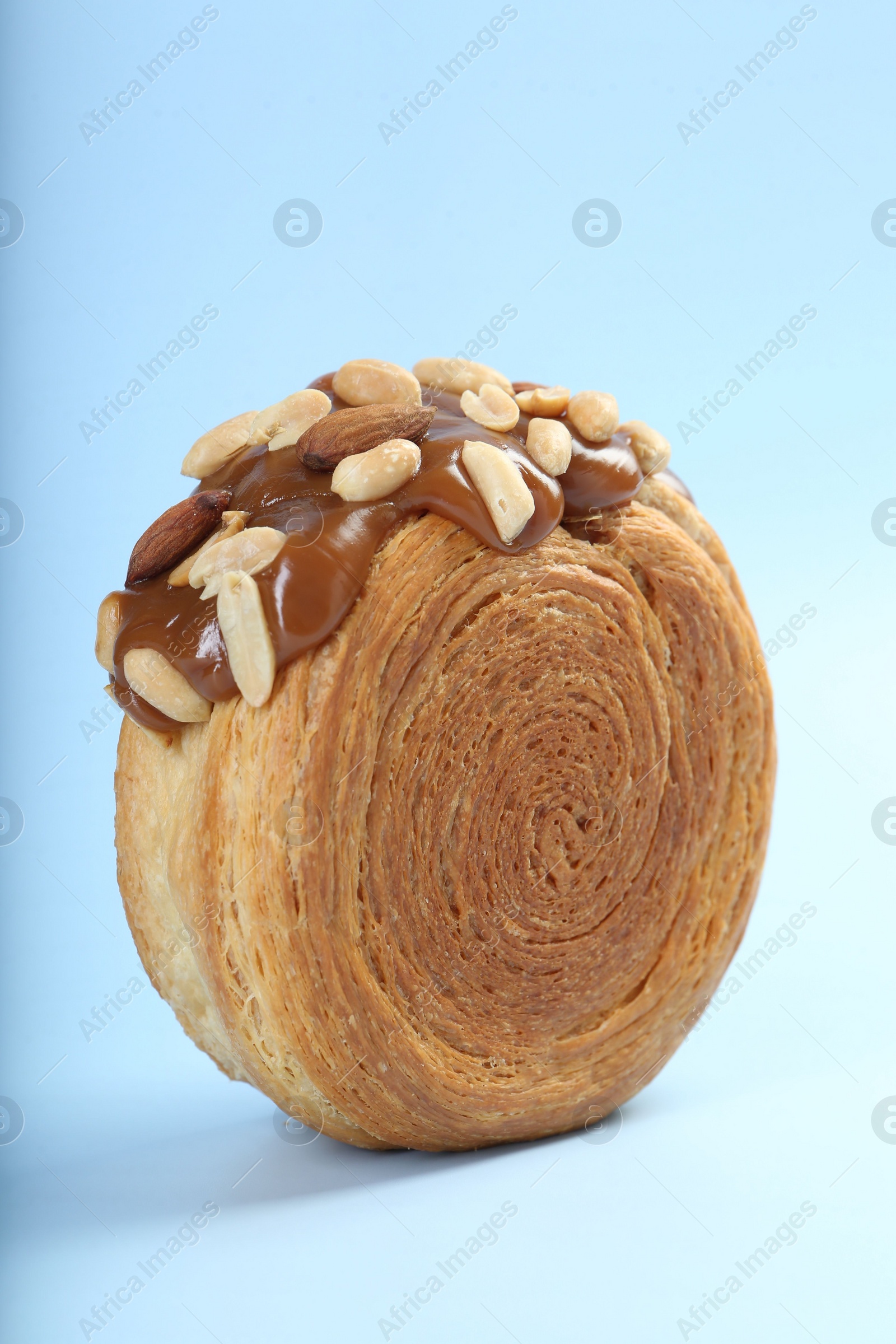 Photo of One supreme croissant with chocolate paste and nuts on light blue background, closeup. Tasty puff pastry