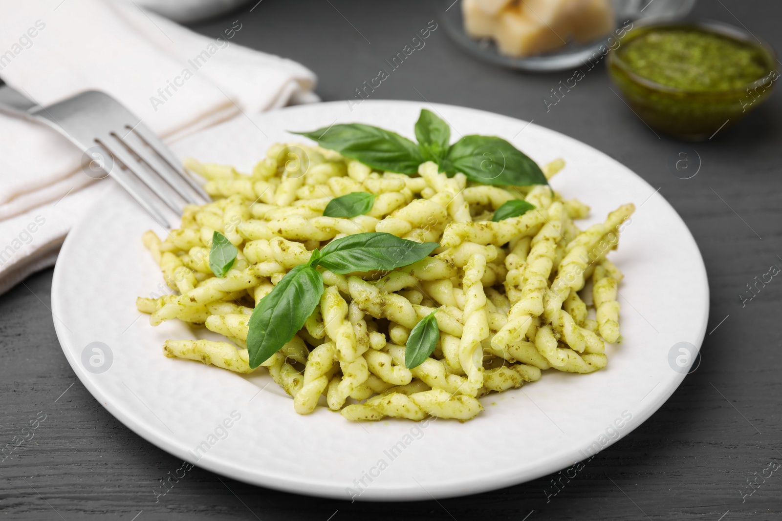 Photo of Plate of delicious trofie pasta with pesto sauce and basil leaves on grey wooden table