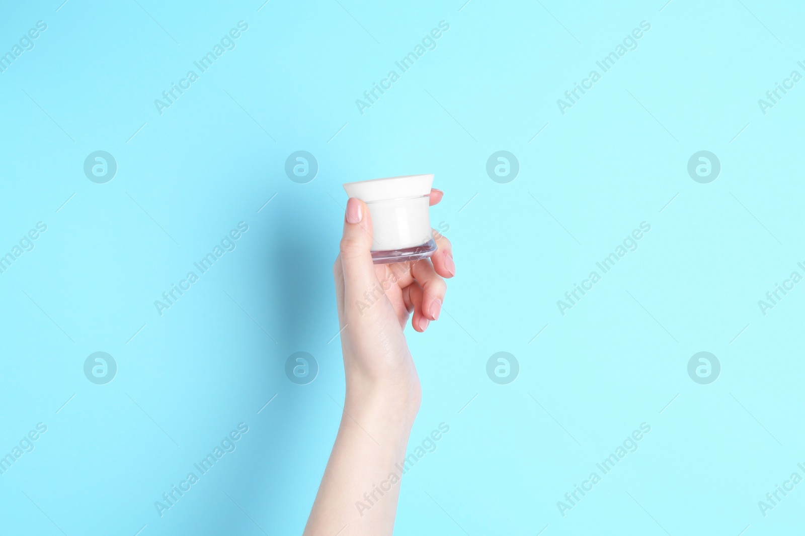 Photo of Woman holding jar of cream on light blue background, closeup