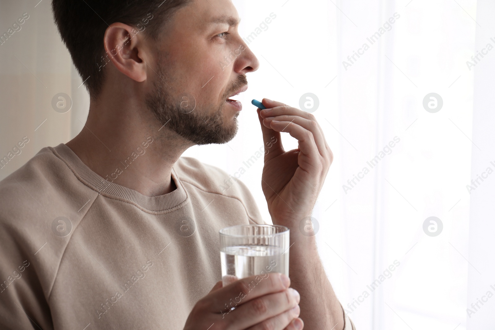 Photo of Man with glass of water taking pill at home