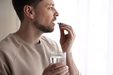 Photo of Man with glass of water taking pill at home