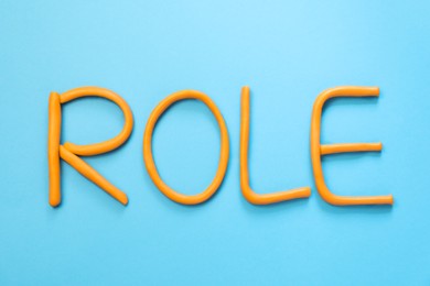 Photo of Word Role made with orange plasticine on light blue background, flat lay