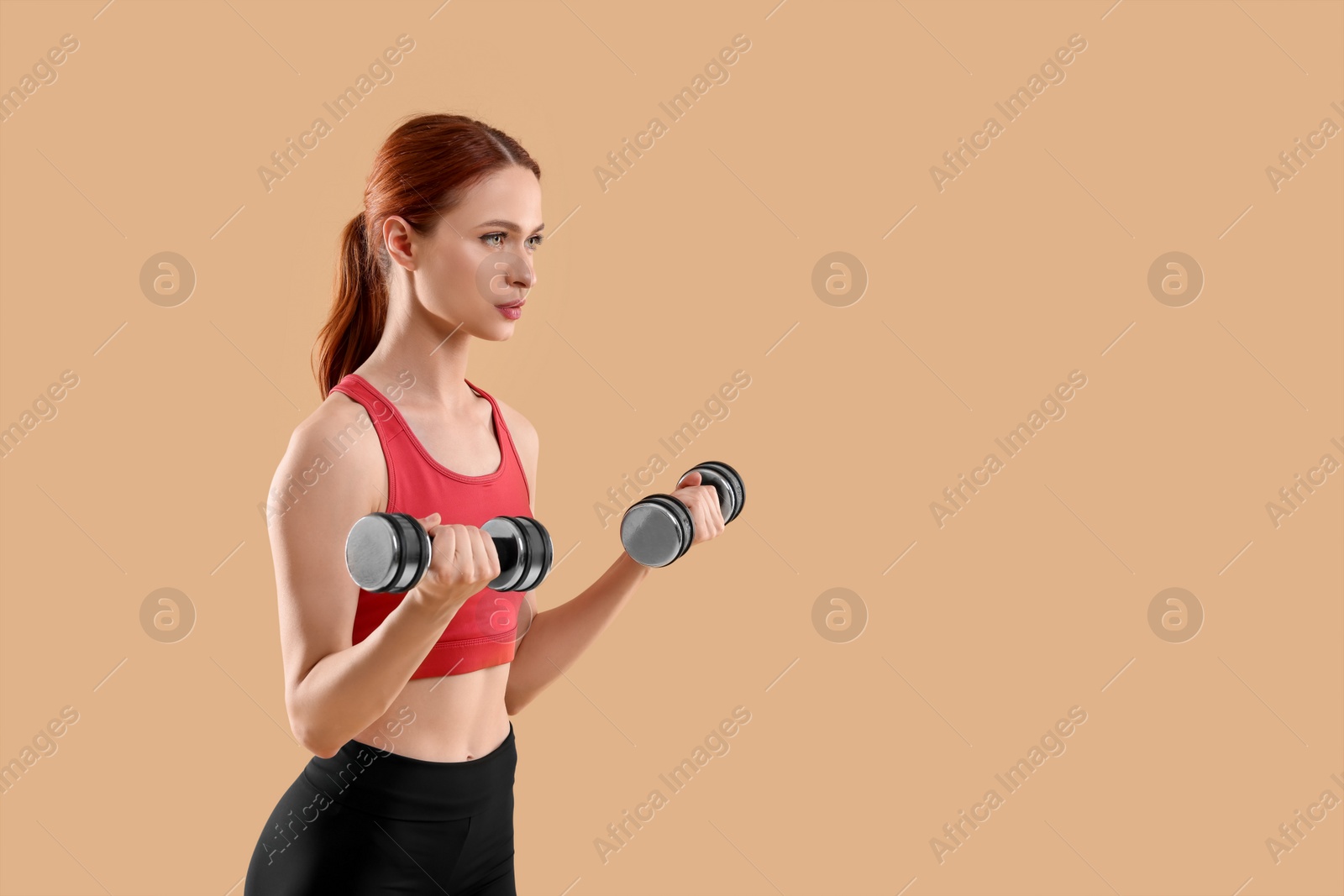 Photo of Young woman in sportswear doing exercises with dumbbells on beige background, space for text