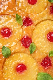 Tasty pineapple cake with cherries and mint as background, top view