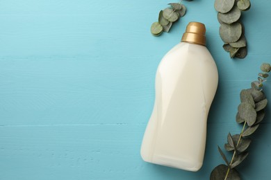 Photo of Bottle of fabric softener and eucalyptus leaves on light blue wooden table, flat lay. Space for text