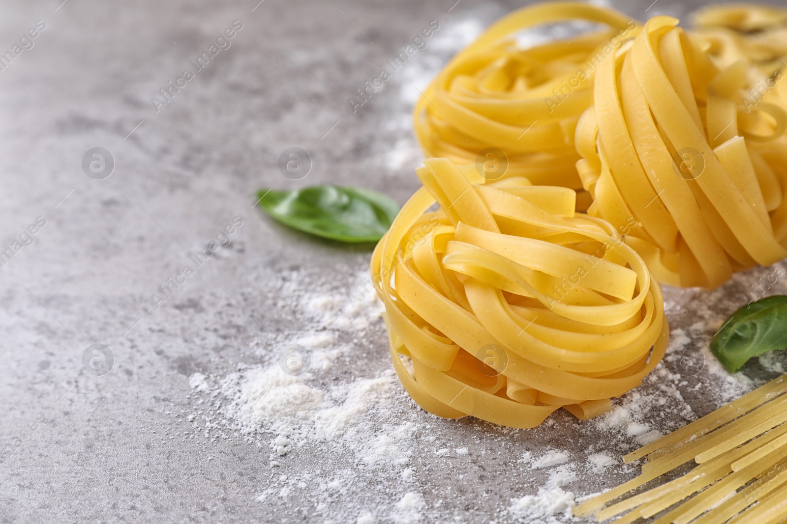 Photo of Uncooked tagliatelle pasta on grey table, closeup. Space for text