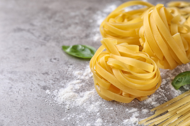 Photo of Uncooked tagliatelle pasta on grey table, closeup. Space for text
