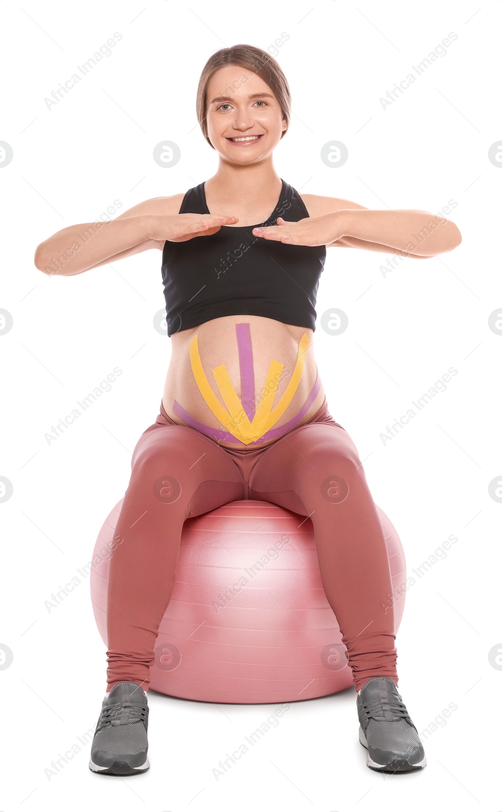 Photo of Sporty pregnant woman with kinesio tapes doing exercises on fitball against white background