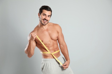 Young man with slim body using measuring tape on grey background. Space for text