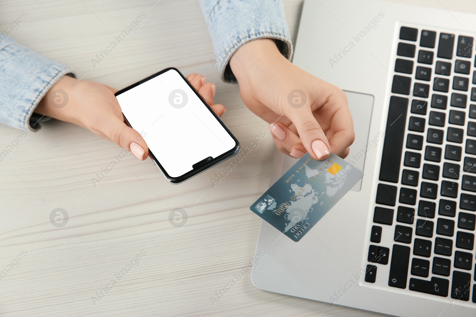 Photo of Online payment. Woman using credit card and smartphone with blank screen near laptop at white wooden table, above view